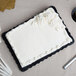 A white frosted cake on a black Enjay cake board on a table.