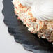 A piece of cake with white frosting and coconut flakes on a black Enjay cake circle.