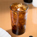 A Cambro amber plastic tumbler filled with brown liquid and ice on a table.