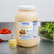 A white container of Ken's Foods Golden Honey Mustard Dressing on a kitchen counter next to a bowl of salad, cherry tomatoes, and lettuce.