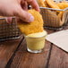 A hand dipping a chicken nugget into a small bowl of Ken's Golden Honey Mustard Dressing.