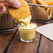 A hand dipping a piece of fried chicken into a small glass of yellow sauce.