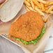 A hand holding a fried chicken sandwich with a breaded chicken breast fillet and french fries.
