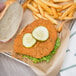 A person holding a breaded fried chicken sandwich with pickles and fries.