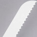 A white plastic Fineline bread knife with a wavy edge.