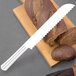 A Fineline white plastic bread knife on a wooden cutting board with a loaf of bread.