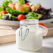 A Ken's Foods jar of white liquid Buttermilk Ranch dressing next to a bowl of salad.