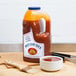 A jug of Sweet Baby Ray's Sweet Red Chili Pepper Wing Sauce and Glaze on a table with a bowl of sauce and a brush.