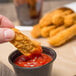 A person dipping a Brakebush Gold'N'Spice Chik'N Fry Strip into a cup of ketchup.