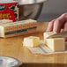 A person cutting a stick of butter on a cutting board.