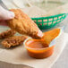 A person dipping Sweet Baby Ray's Buffalo Wing Sauce into a piece of fried chicken.