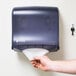 A hand pulling a paper towel out of a San Jamar Ultrafold Fusion paper towel dispenser on a wall.