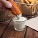 A person dipping a piece of fried food into a small bowl of white sauce.