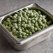 A metal container filled with frozen peas on a table.