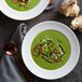 A table set with two bowls of green pea soup with onion rings and bread.