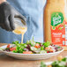 A gloved hand pouring Wish-Bone Italian Dressing on a salad.