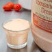 A small glass cup with a creamy orange liquid next to a large jar of creamy orange liquid.
