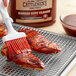 A person using a brush to put Cattlemen's Kansas City Classic BBQ Sauce on barbecued meat on a rack.