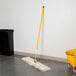 A Lavex all-in-one dry mop with a yellow handle in a room with a mop and bucket.