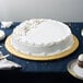 A white cake on a table with a gold round cake drum underneath.