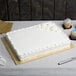 A white cake on an Enjay gold 1/2 sheet cake board on a table.