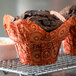 A chocolate muffin in a red and white Enjay Mariposa baking cup on a metal cooling rack.