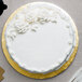 A white cake with white frosting and flowers on a gold Enjay round cake drum.