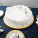 An Enjay gold round cake drum under a white cake on a table.