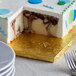 A slice of cake with blue and white icing on a gold square cake drum with a white background.