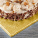 A cake with frosting and pecans on a gold Enjay square cake drum.