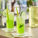 Two glasses of green Finest Call lime drinks with straws and lime slices on a bar counter.