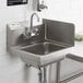 A Regency stainless steel hand sink with a faucet and white tile wall.