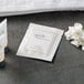 A white package of Novo Essentials makeup remover wipes with a white label next to a white flower.