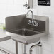 A Regency stainless steel hand sink with a faucet above it on a counter with a hand towel and soap dispenser.