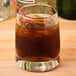 A Libbey rocks glass filled with brown liquid, ice, and a straw.