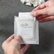 A person holding a white package of Novo Essentials Hotel and Motel Makeup Remover Wipes.