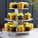 An Enjay 3-tier silver cupcake stand with cupcakes on a table.
