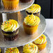 A Enjay 3-tier silver cupcake stand holding cupcakes with yellow frosting and sprinkles.