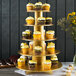 A gold Enjay 5-tier cupcake stand with cupcakes decorated with yellow frosting and sprinkles.