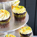 A cupcake with yellow frosting and sprinkles on a silver tray.