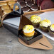 A black Enjay cupcake box with a tulip design containing a cupcake with yellow frosting and sprinkles.