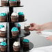 A person putting cupcakes on a black tiered cupcake stand.