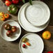 A group of Oneida Marble porcelain plates with raised rims on a wood table with bowls of tomatoes.