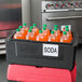 A black Metro Mightylite BigBoy food pan carrier with a red lid holding bottles of orange liquid.