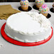 A white cake with frosting on an Enjay red round cake drum on a table.
