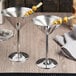 Two Tablecraft stainless steel martini glasses filled with olives on a counter.