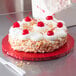 A cake with whipped cream and cherries on a red Enjay round cake drum.