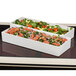 Two rectangular Bon Chef trays filled with salad and vegetables on a table in a salad bar.