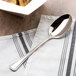 A Oneida Needlepoint stainless steel serving spoon on a napkin next to a bowl of food.