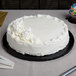 A white cake on an Enjay black round cake drum on a table with a knife and candles.